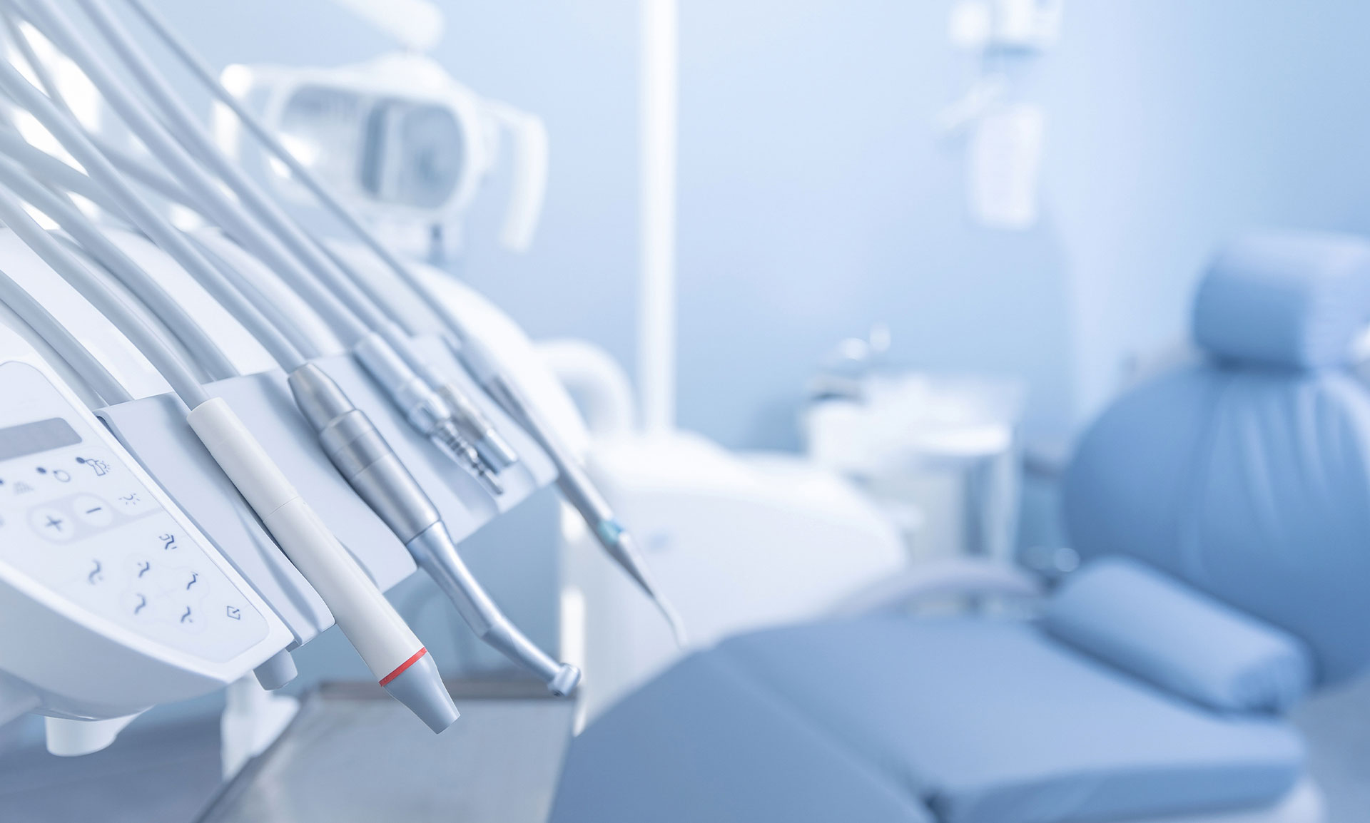The image shows a modern dental office setting with various equipment and chairs visible, including dental chairs, a dental table, and medical instruments such as drills and probes.