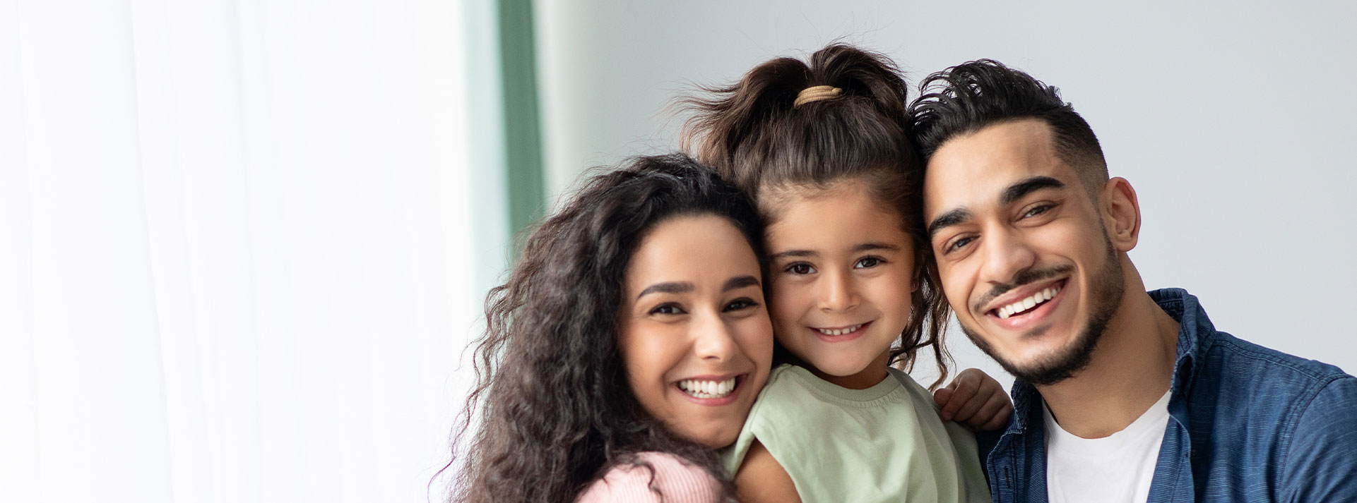 A family of four, including two adults and two children, smiling together with one adult holding a child.